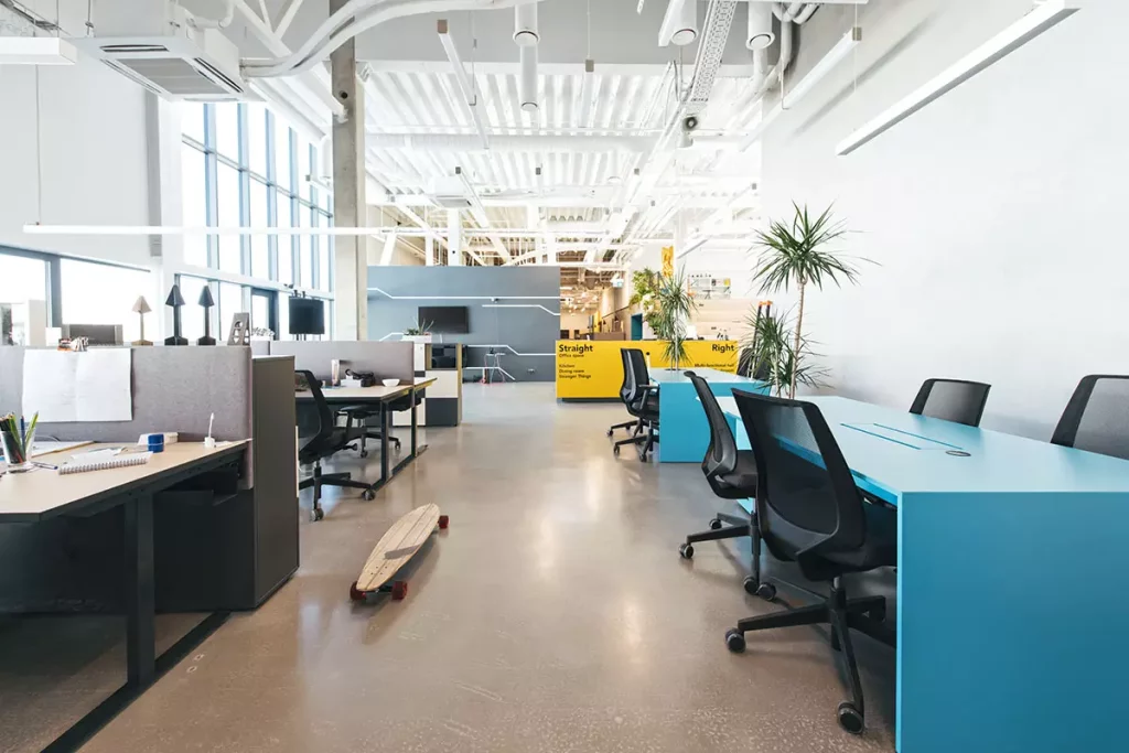 An office space featuring grey, blue, and yellow desks, a wooden penny board, and indoor plants. A virtual office solution in Singapore likely has this layout for its coworking space service