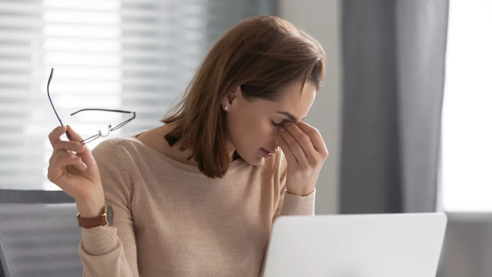 A lady on a laptop having a migraine due to challenges associated with a virtual office space in Singapore