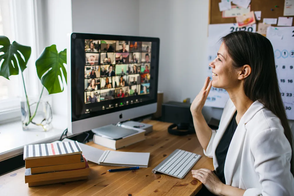 Lady waving to a Zoom meeting room full of participants. A company using a virtual office space in Singapore relies on remote teams.