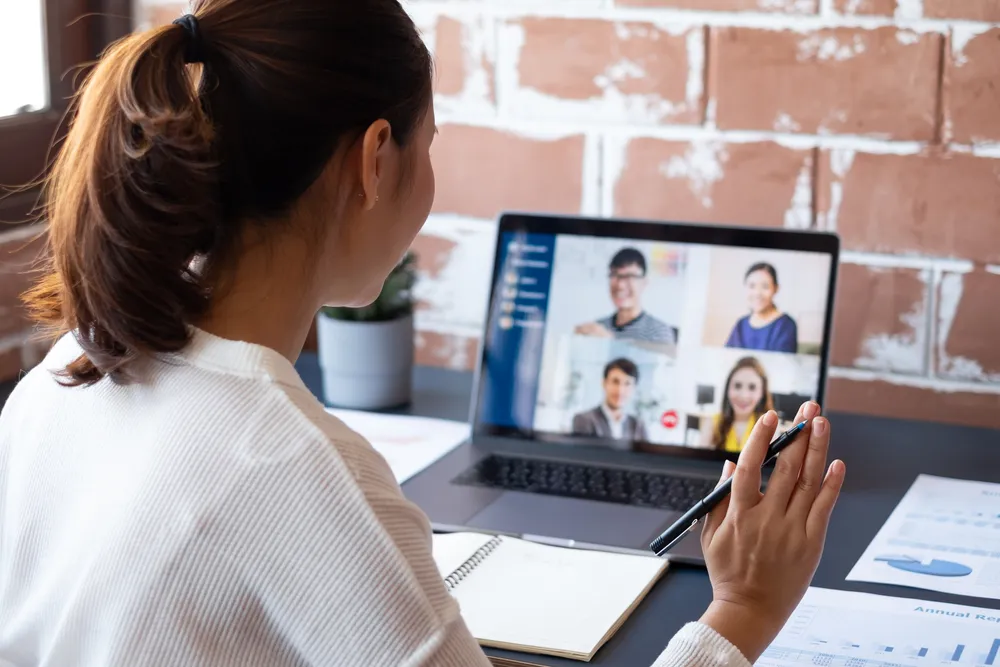 A lady has an ongoing Zoom meeting, waving to the people on-screen, a typical setup when working with a virtual office space in Singapore