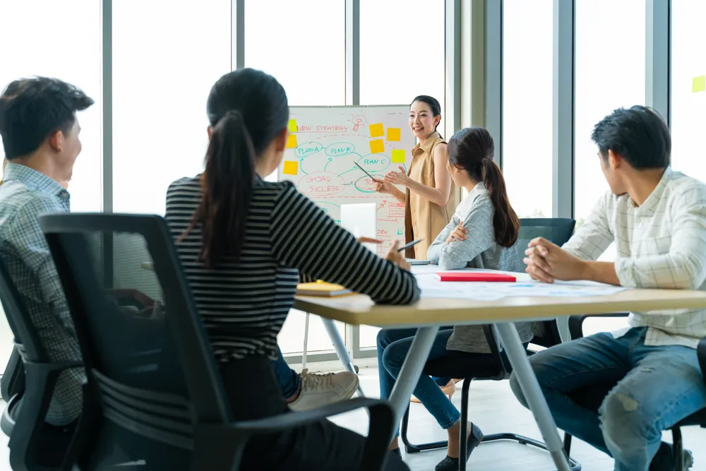 Employees collaborating over a whiteboard in the workplace. A virtual office in Singapore is often assumed to be a physical workplace when it's not.