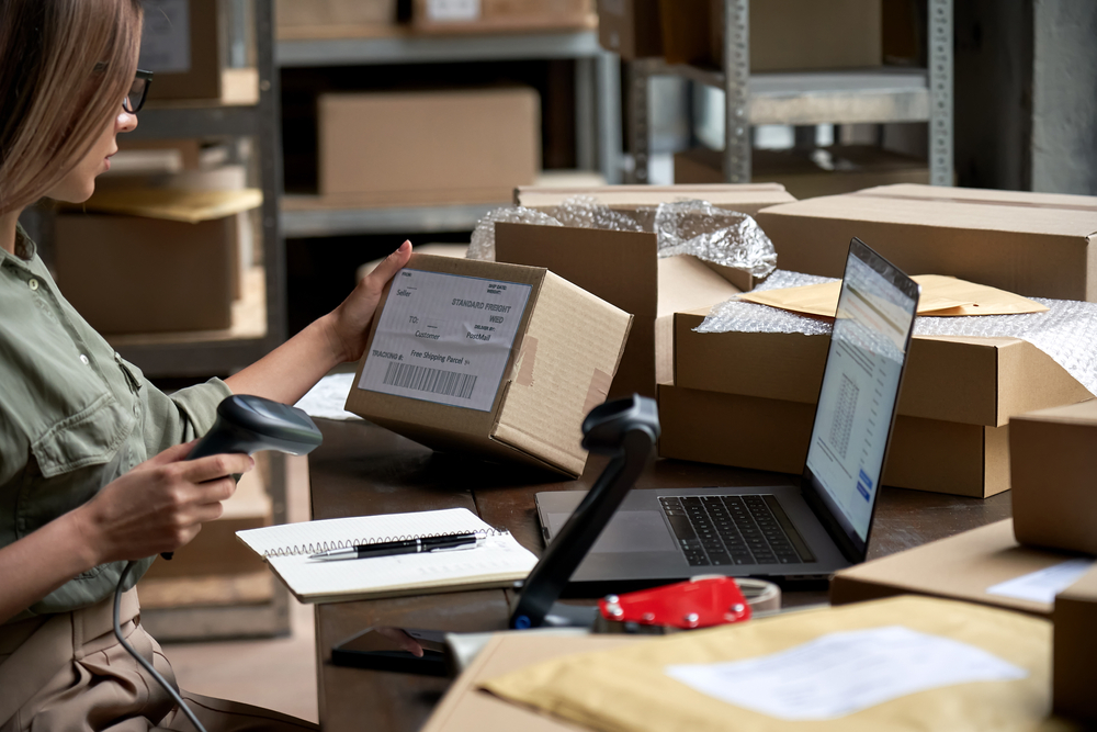 Female warehouse worker scanning barcodes and managing inventories of goods packaged in boxes. A virtual office solution in Singapore can't be a warehouse or fulfillment center.