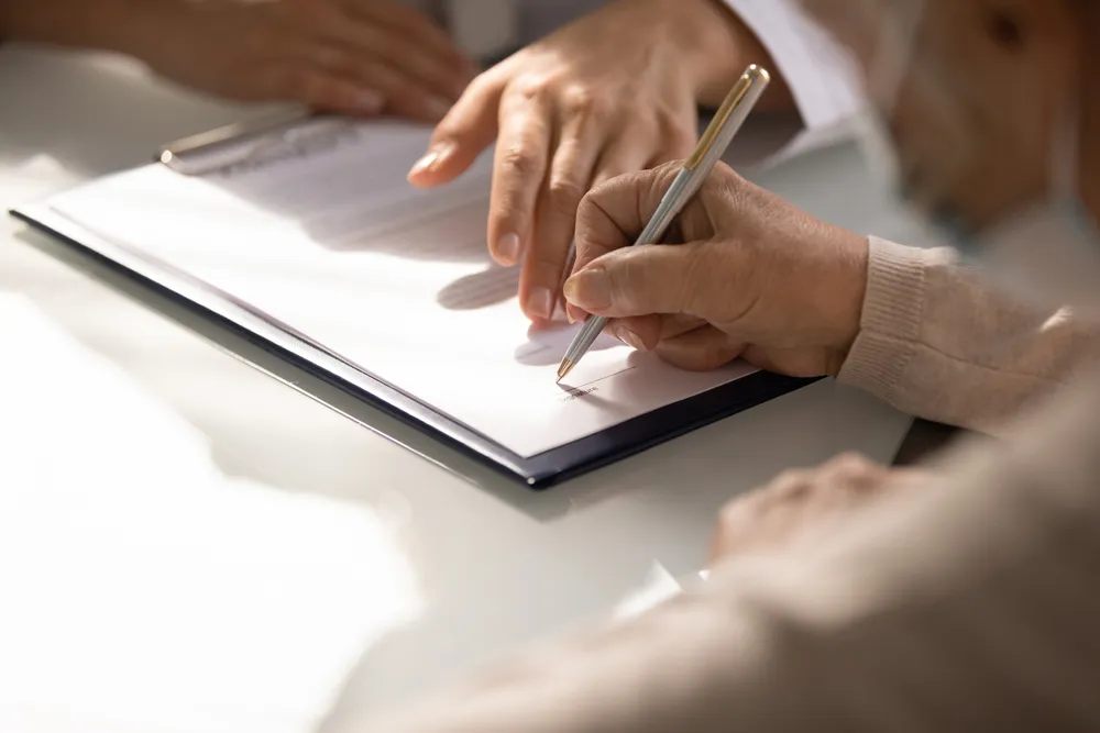 A man signing the bottom portion of a clipboard, indicating filling out a form. When filling out a ACRA registration, it's best if the virtual office in Singapore you're partnered with is ACRA-compliant