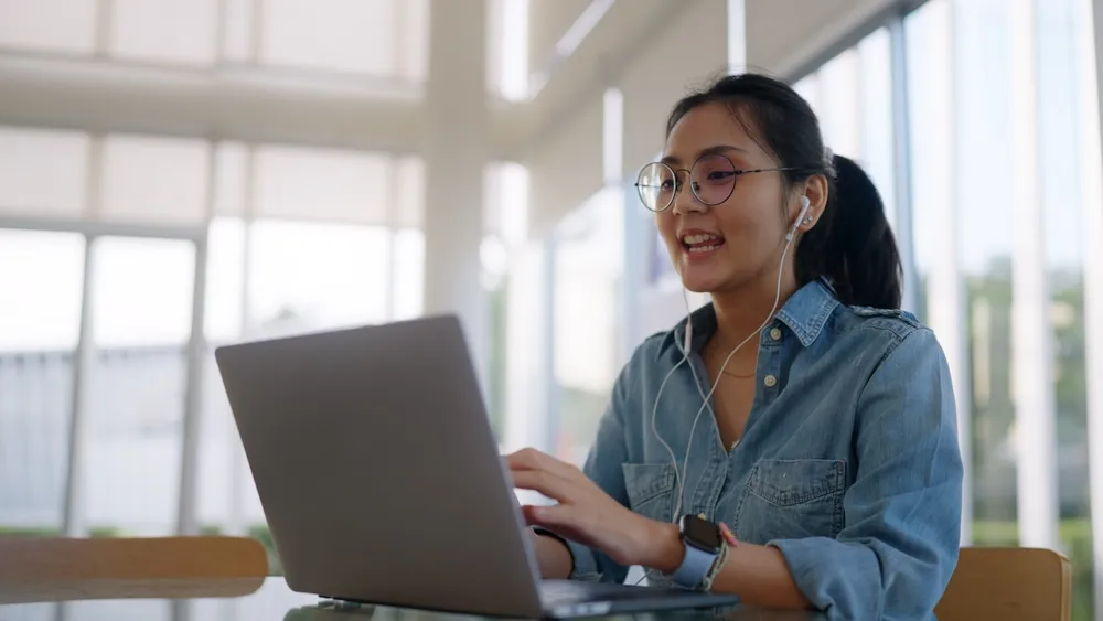 Lady with earphones and denim shirt using and speaking into the laptop, a common scenario for a virtual office in Singapore