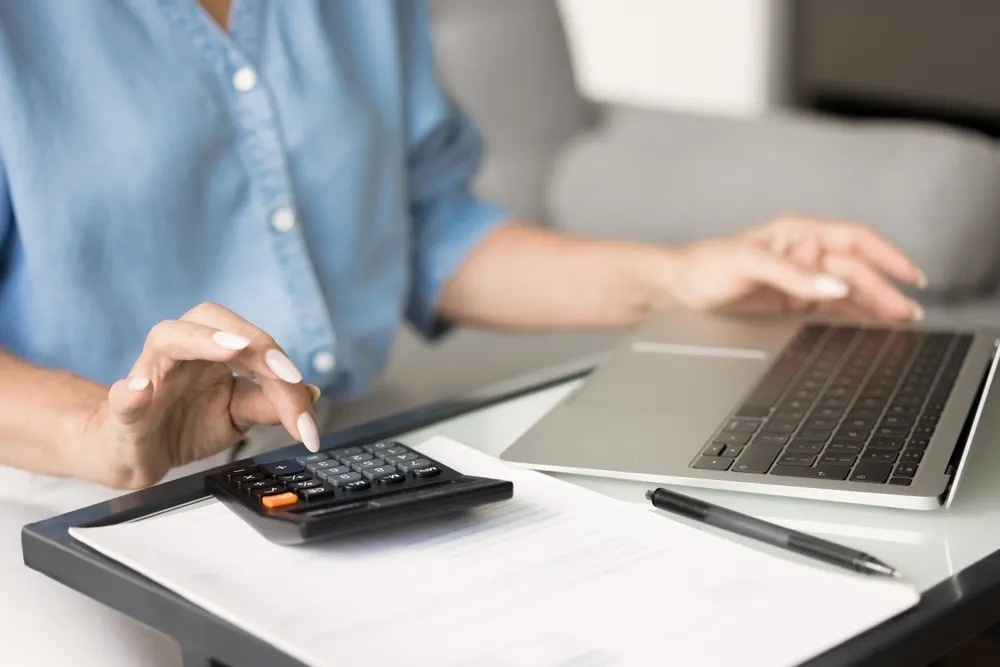 Lady calculating business expenses on a laptop using a calculator; comparing the costs of a virtual office in Singapore with a traditional office.
