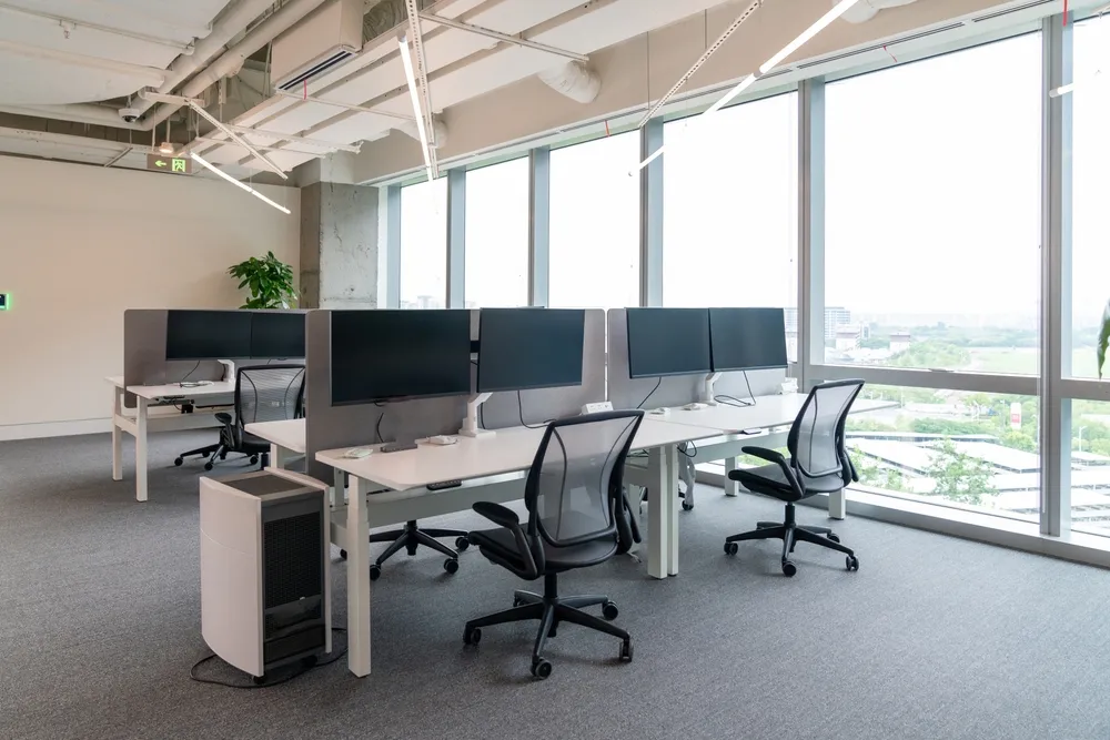 Work terminals on a coworking table in a grey office scheme. A virtual office in Singapore doesn't require founders to furnish their company with these tools.