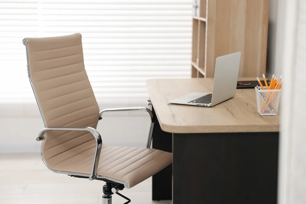 A minimalist personal work desk featuring a beige chair, desk, a laptop, and a container of pencils, a setup ideal for working with a virtual office space in Singapore